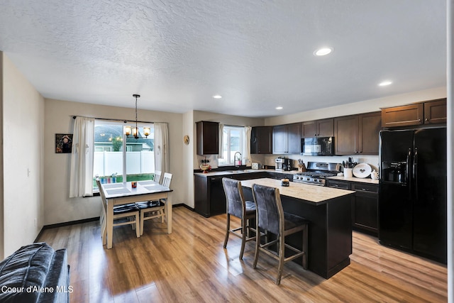 kitchen with a breakfast bar, decorative light fixtures, a center island, black appliances, and light wood-type flooring