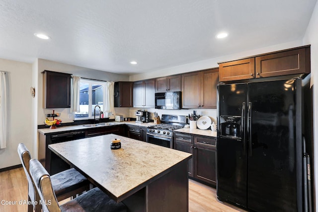 kitchen with sink, light wood-type flooring, a kitchen breakfast bar, a kitchen island, and black appliances