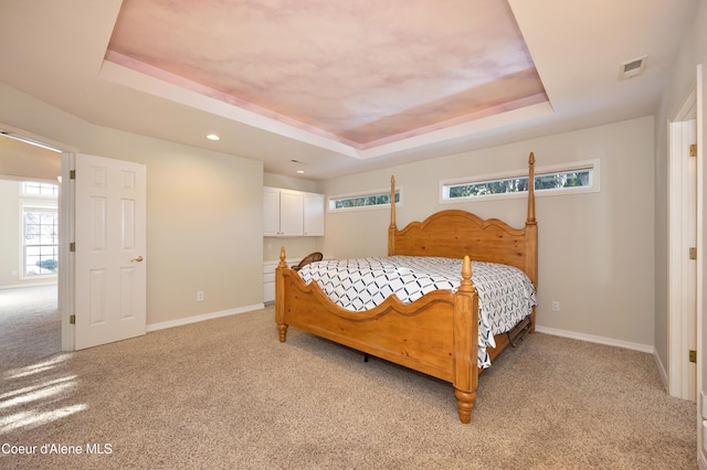 bedroom with a raised ceiling, light carpet, and multiple windows