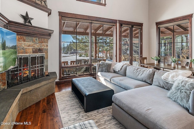 living room featuring hardwood / wood-style flooring, a stone fireplace, and a high ceiling