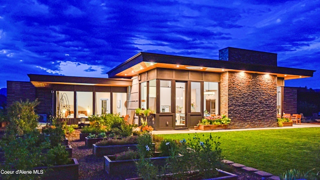 back house at dusk featuring a yard and a sunroom