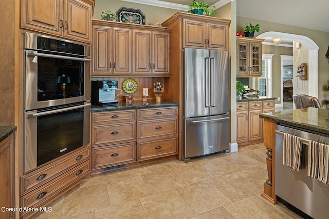 kitchen with stainless steel appliances, crown molding, and dark stone countertops