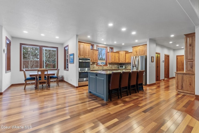 kitchen featuring light hardwood / wood-style flooring, a breakfast bar, stainless steel appliances, a kitchen island, and dark stone counters