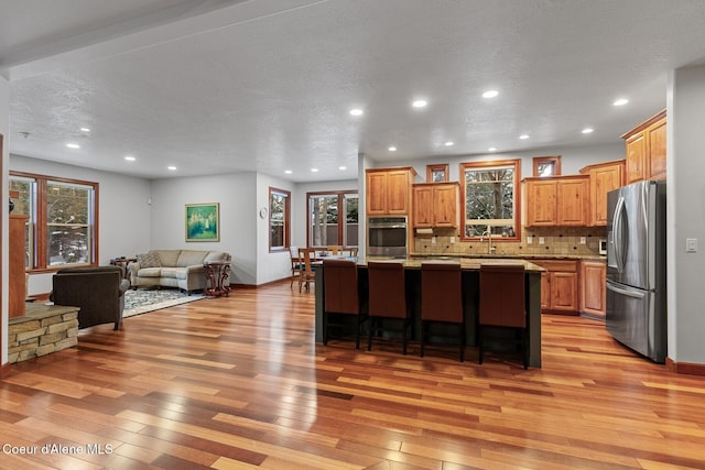 kitchen with a sink, a kitchen island, light wood-style floors, open floor plan, and appliances with stainless steel finishes