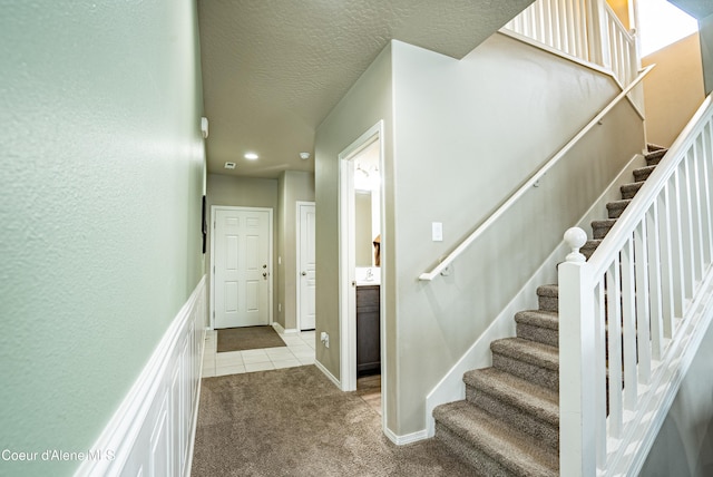 stairway featuring a textured ceiling, tile patterned floors, carpet flooring, and baseboards