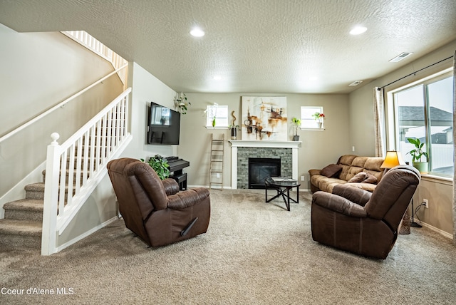 living room featuring carpet, visible vents, a stone fireplace, and stairs