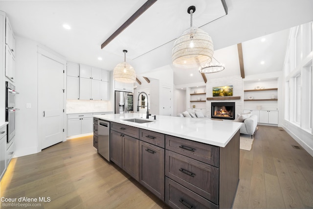 kitchen featuring pendant lighting, wood-type flooring, sink, a kitchen island with sink, and dark brown cabinets