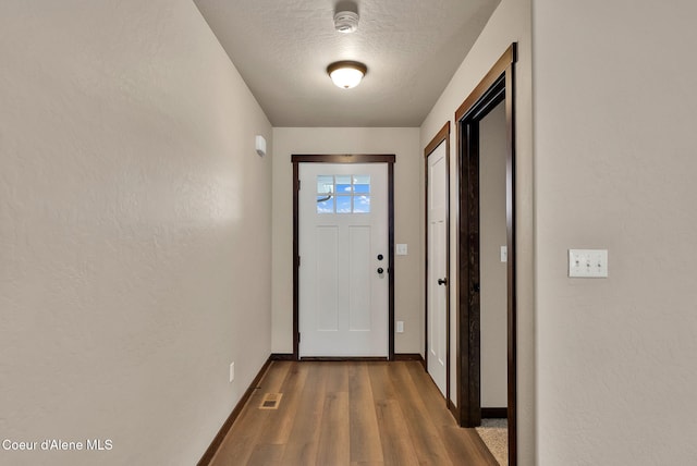 doorway to outside with visible vents, dark wood finished floors, a textured ceiling, and baseboards