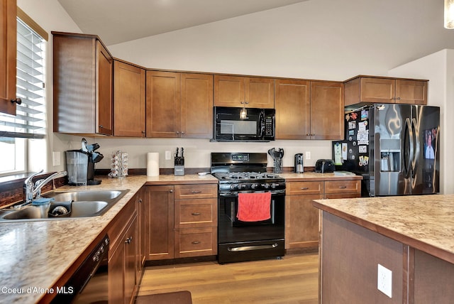 kitchen with lofted ceiling, light countertops, light wood-style floors, a sink, and black appliances