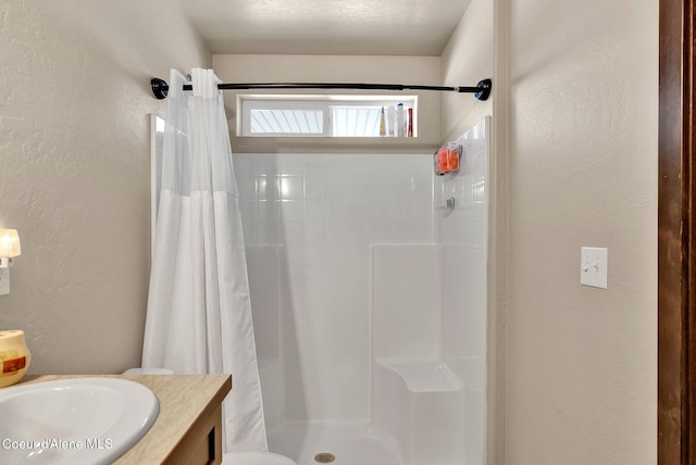 bathroom featuring a textured ceiling, a textured wall, a shower stall, and vanity