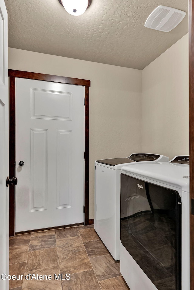 clothes washing area with a textured ceiling, laundry area, and washing machine and dryer