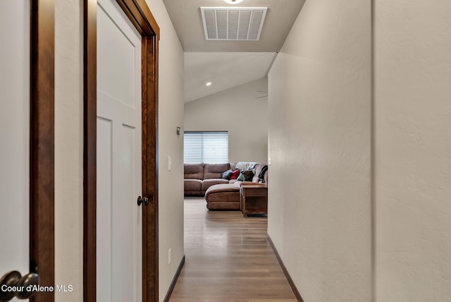 corridor with vaulted ceiling, wood finished floors, visible vents, and baseboards