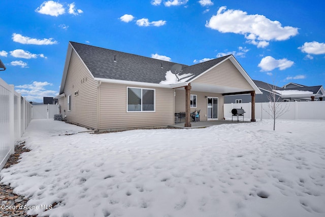 snow covered back of property with roof with shingles and a fenced backyard