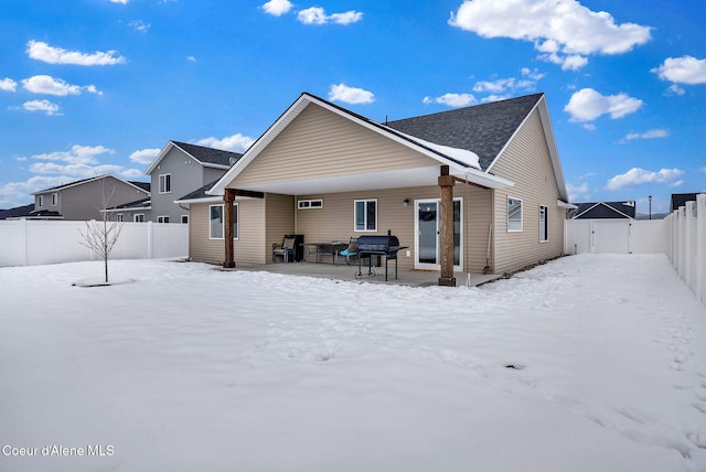 snow covered house featuring a gate, a fenced backyard, and a patio