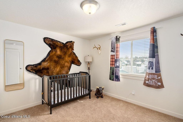 carpeted bedroom featuring a textured ceiling and a crib