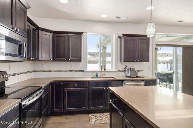 kitchen featuring sink, decorative light fixtures, dark brown cabinets, stainless steel appliances, and backsplash