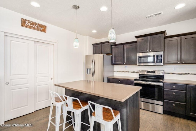 kitchen featuring appliances with stainless steel finishes, hanging light fixtures, a center island, a kitchen bar, and dark hardwood / wood-style flooring