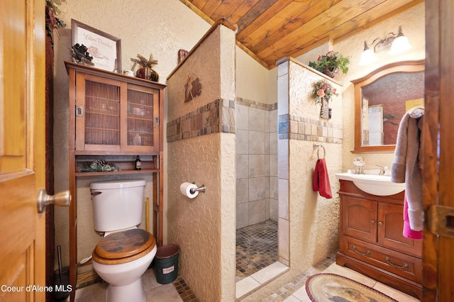 bathroom with wood ceiling, a tile shower, vanity, vaulted ceiling, and toilet