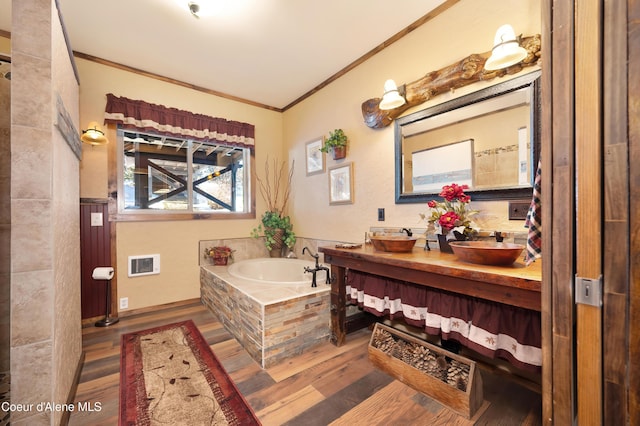 bathroom featuring hardwood / wood-style flooring, crown molding, a relaxing tiled tub, and vanity