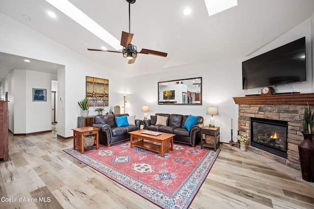 living area with vaulted ceiling with skylight, a stone fireplace, light wood finished floors, and recessed lighting