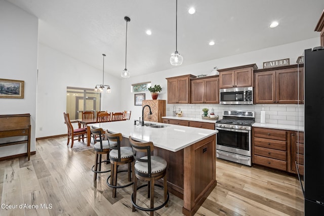 kitchen featuring tasteful backsplash, appliances with stainless steel finishes, a sink, an island with sink, and light wood-type flooring