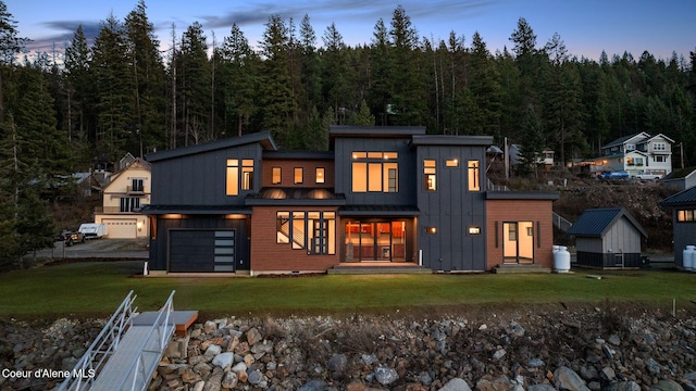 back house at dusk featuring a garage and a yard