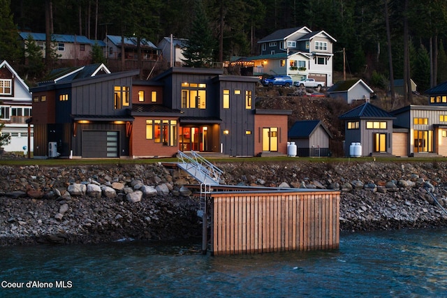 rear view of house featuring a standing seam roof, a garage, a water view, board and batten siding, and metal roof