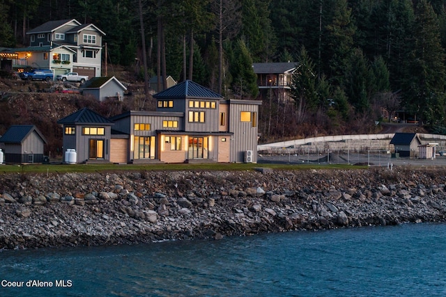 rear view of property featuring a standing seam roof, a water view, board and batten siding, brick siding, and metal roof