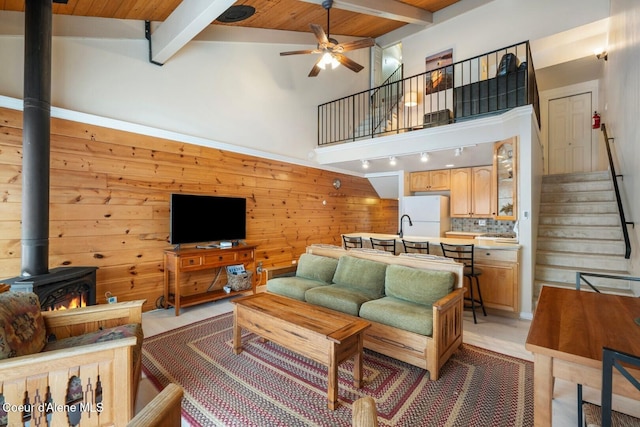 living area with beam ceiling, stairway, a wood stove, wood walls, and ceiling fan