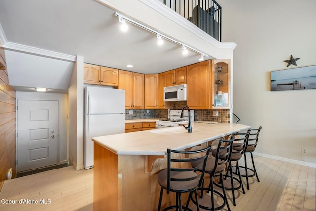 kitchen featuring a peninsula, white appliances, light countertops, and a kitchen breakfast bar