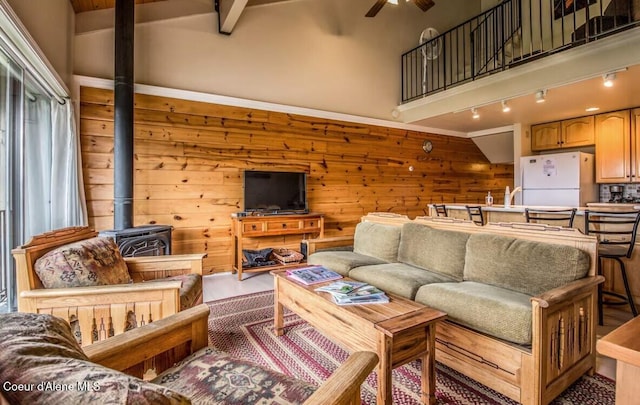 living area featuring rail lighting, a ceiling fan, a wood stove, wooden walls, and high vaulted ceiling