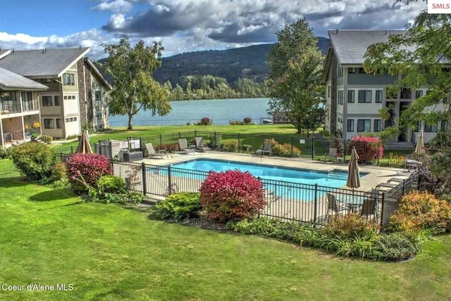 community pool featuring a lawn, fence, and a water and mountain view