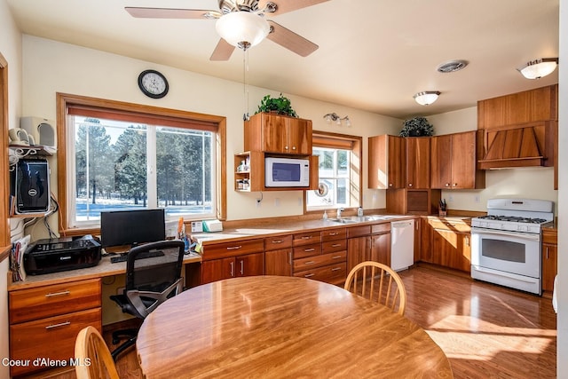 kitchen featuring sink, custom exhaust hood, white appliances, light hardwood / wood-style flooring, and ceiling fan