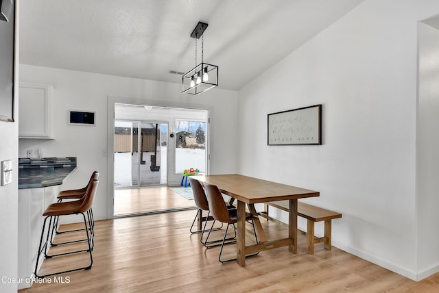 dining area featuring light wood-type flooring, vaulted ceiling, and a notable chandelier