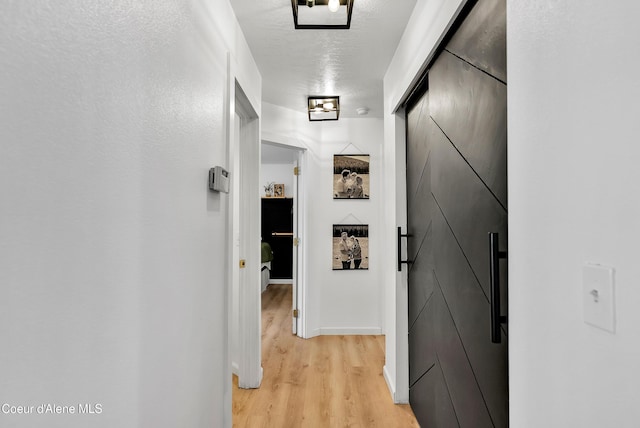 hall with a barn door, light hardwood / wood-style floors, and a textured ceiling