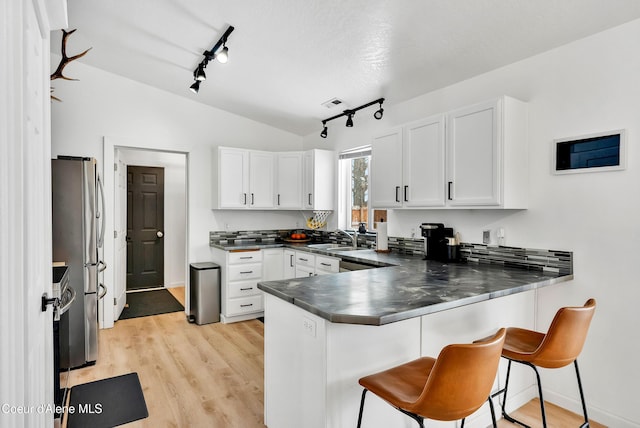 kitchen featuring white cabinetry, kitchen peninsula, a breakfast bar area, and stainless steel fridge