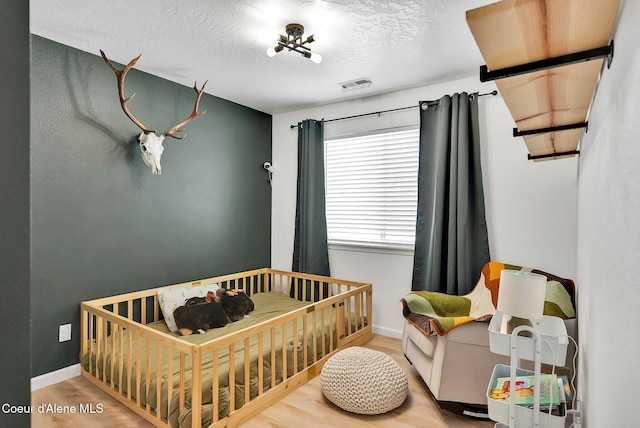 bedroom featuring a crib, wood-type flooring, and a textured ceiling