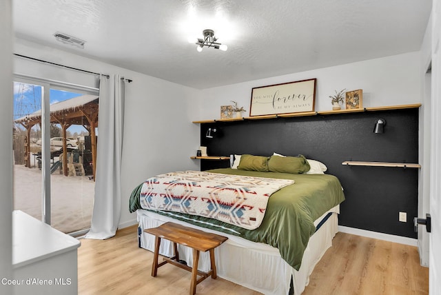 bedroom featuring a textured ceiling, access to exterior, and light hardwood / wood-style flooring