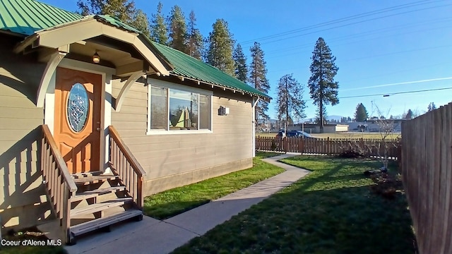 view of side of property featuring a standing seam roof, fence, metal roof, and a lawn