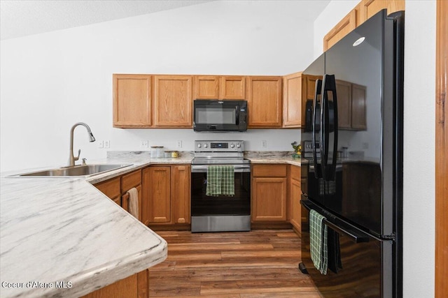 kitchen with dark wood-style floors, vaulted ceiling, light countertops, black appliances, and a sink