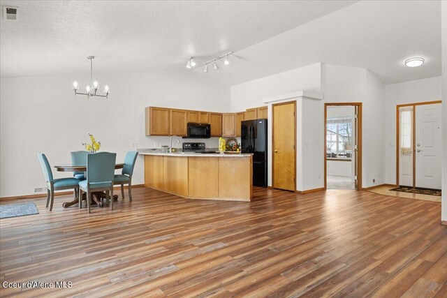 kitchen with light wood-style flooring, a peninsula, light countertops, black appliances, and pendant lighting