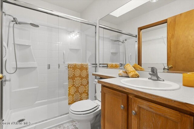 bathroom featuring toilet, a shower with door, a skylight, and vanity