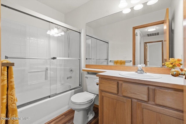 full bath featuring toilet, wood finished floors, vanity, visible vents, and combined bath / shower with glass door