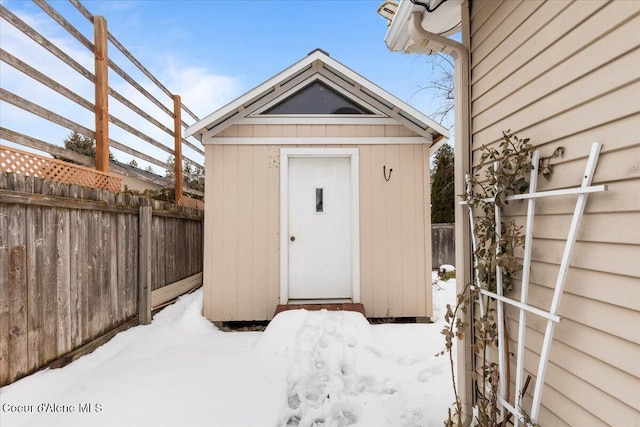 snow covered structure with a storage shed, a fenced backyard, and an outdoor structure