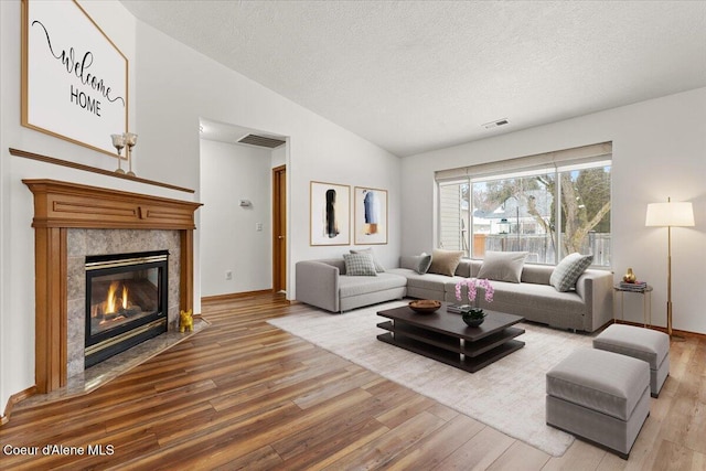 living room with a fireplace, vaulted ceiling, a textured ceiling, and wood finished floors