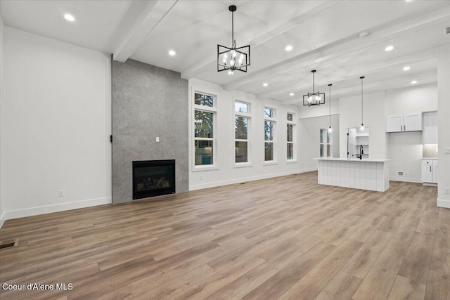 unfurnished living room with light wood-type flooring, an inviting chandelier, vaulted ceiling with beams, and a fireplace