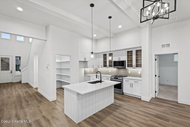 kitchen with sink, a towering ceiling, hanging light fixtures, an island with sink, and gas range