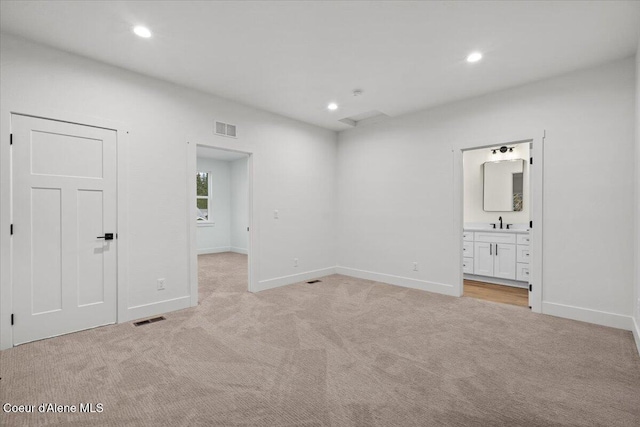 unfurnished bedroom featuring sink, light colored carpet, and ensuite bath