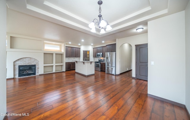 unfurnished living room featuring dark wood finished floors, a tray ceiling, a glass covered fireplace, arched walkways, and a notable chandelier