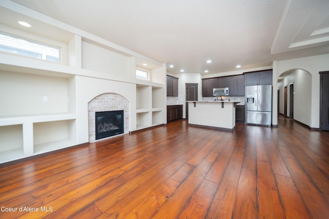 unfurnished living room with built in features, recessed lighting, a fireplace, dark wood-style flooring, and arched walkways